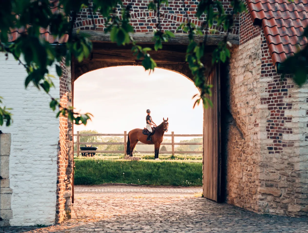 Horse rider posing in front of a brick barn gate at sunset