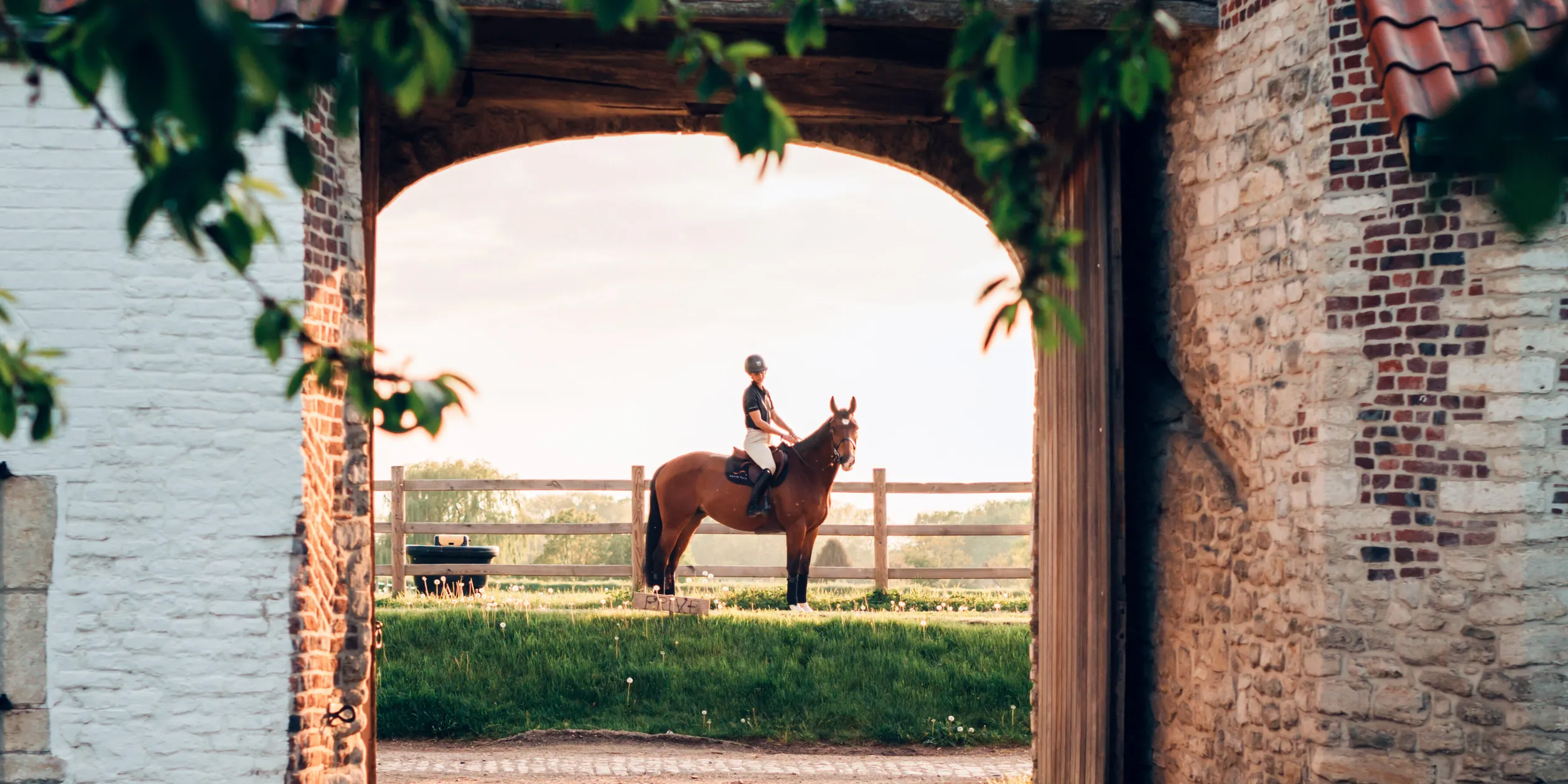 Horse rider posing in front of a brick barn gate at sunset